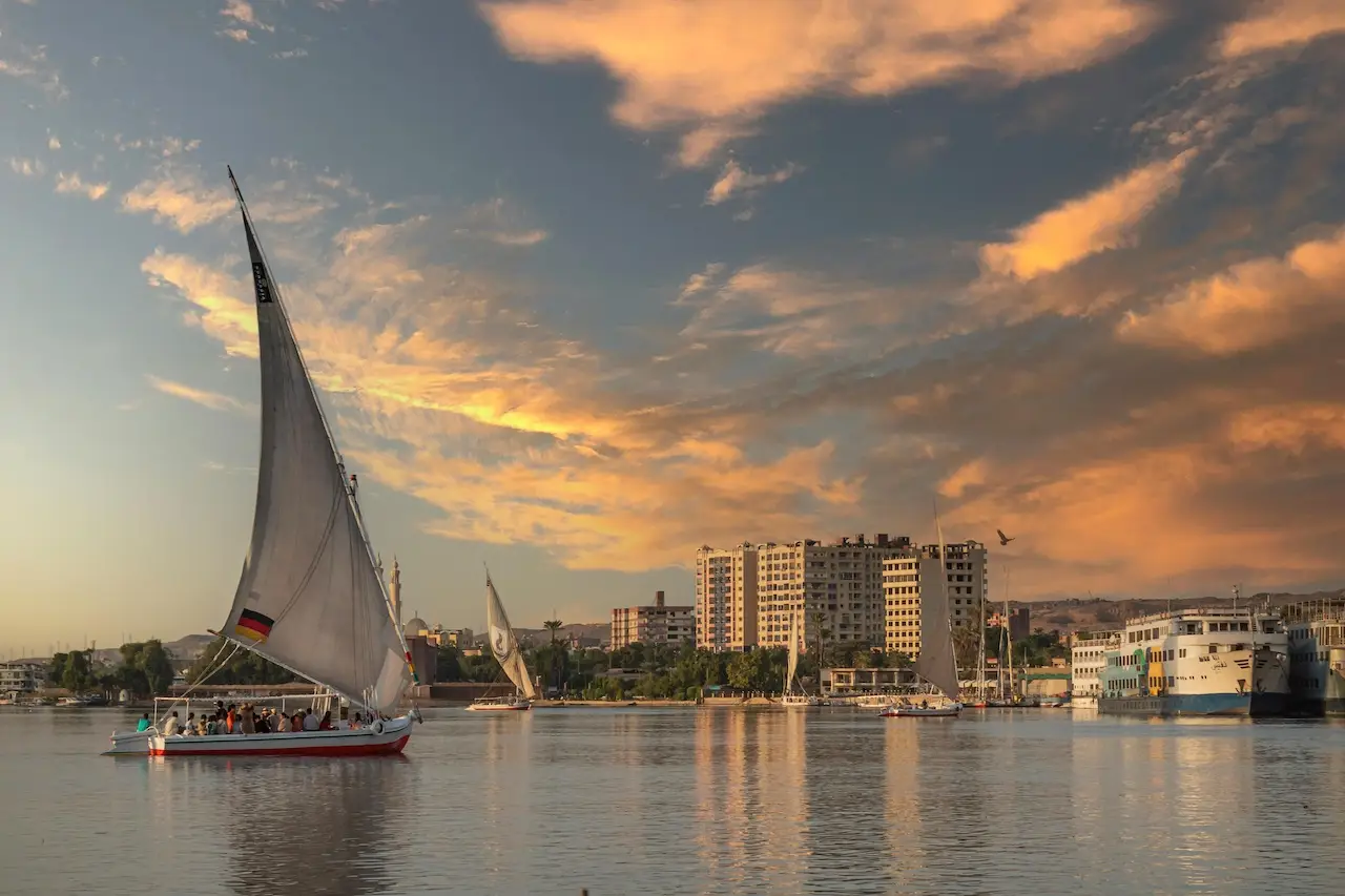 Scenic view of the Nile River in Cairo with a traditional boat sailing past the city skyline under a clear sky